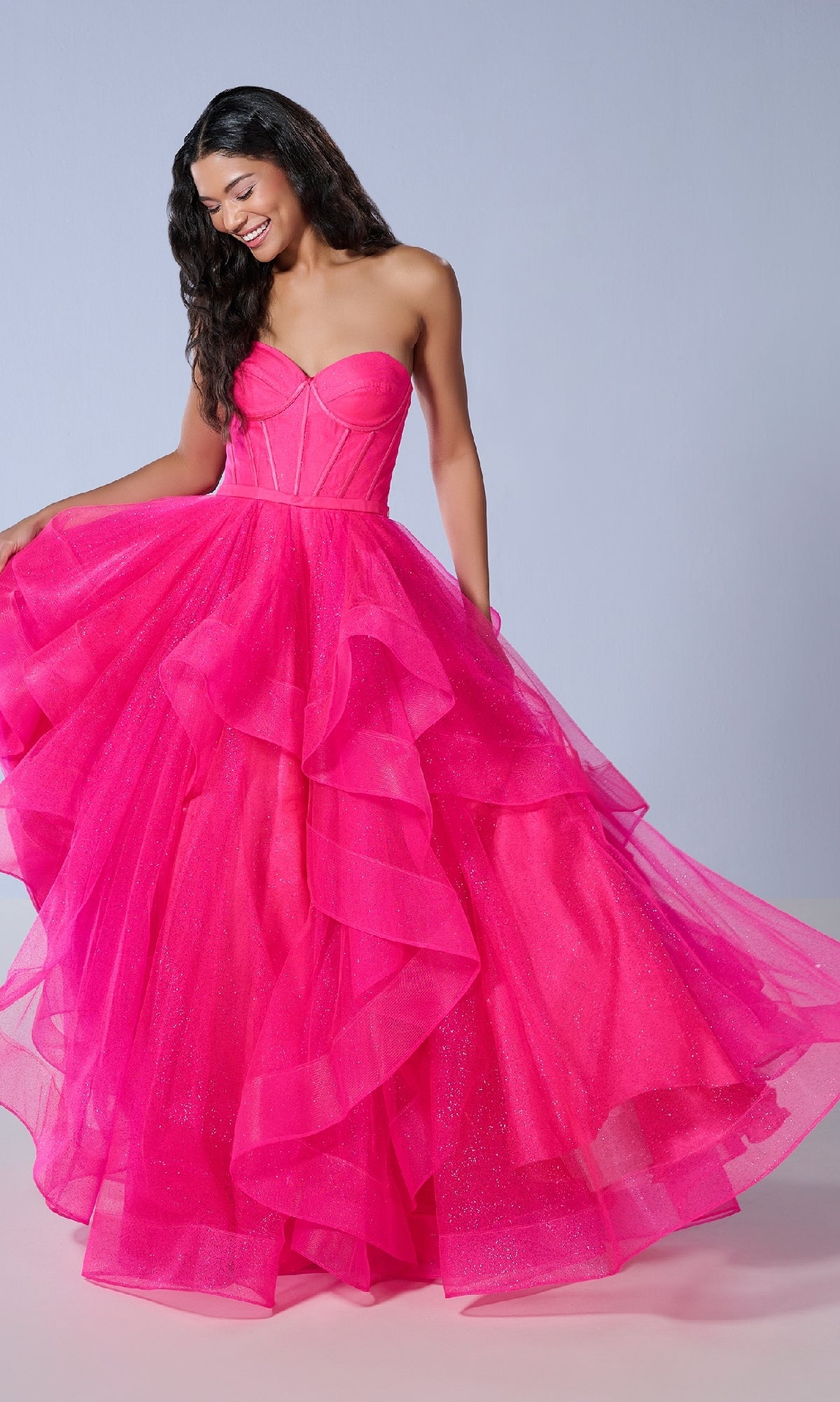 A woman models the Tiffany 16245 long prom dress, featuring a strapless fitted corset bodice and layered glitter tulle skirt, standing against a plain light background.